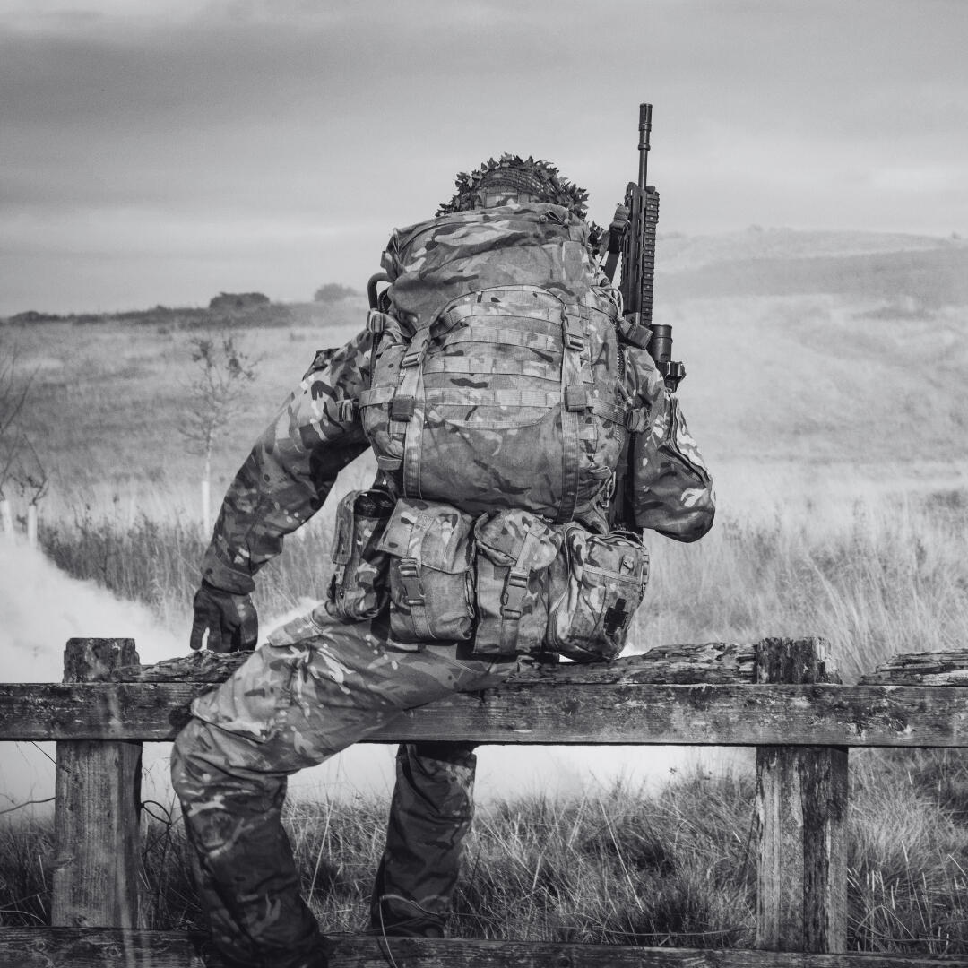 soldier climbing over fence carrying kit